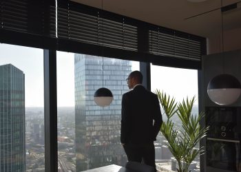 'The Mid-Year CEO Audit: 10 Questions Every UAE Business Leader Should Ask Themselves on June 30' : Image shows a businessman in a black suit looks out at skyscrapers from an office window, embracing an urban view.